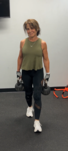 Woman over 50 smiling while carrying two kettlebells in a farmers walk