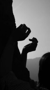 Black and white silhouette of two open, curled hands reaching toward a bright sky, with a mountain outline behind them.